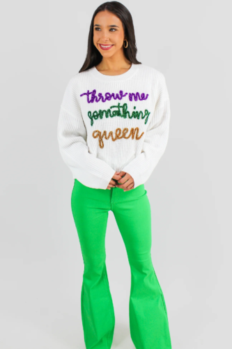 Casual Mardi Gras outfit with a white sweater that reads Throw Me Something Queen, paired with bright green flares