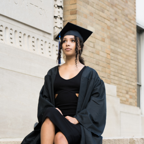 Black woman wearing a graduation cap and gown with her hair styled into a low ponytail with curly pieces in the front
